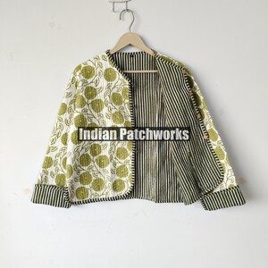 May include: Reversible quilted jacket with a floral pattern on one side and vertical stripes on the other. The jacket features a round collar and long sleeves with striped cuffs. The jacket is hanging on a wooden hanger.