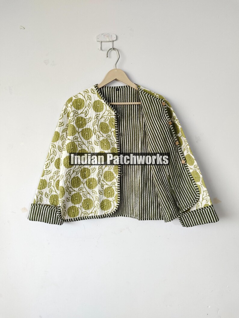 May include: Reversible quilted jacket with a floral pattern on one side and vertical stripes on the other. The jacket features a round collar and long sleeves with striped cuffs. The jacket is hanging on a wooden hanger.