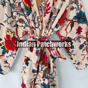 May include: A white robe with a floral print in shades of red, blue, green, and yellow. The robe has a long sleeve and a tie belt. The text "Indian Patchworks" is visible on the robe.