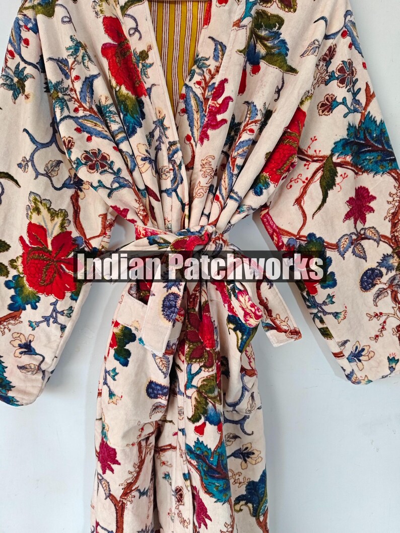 May include: A white robe with a floral print in shades of red, blue, green, and yellow. The robe has a long sleeve and a tie belt. The text "Indian Patchworks" is visible on the robe.