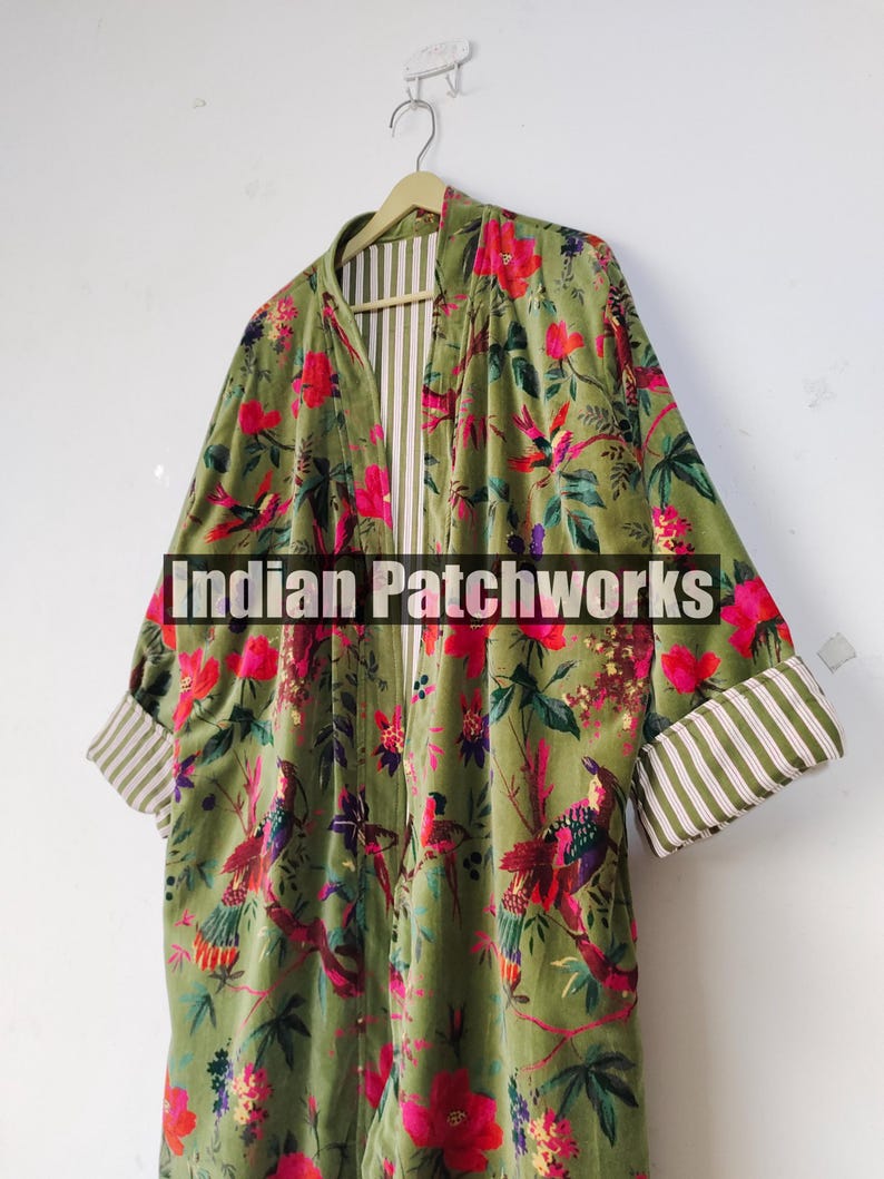 Puede incluir: Una bata larga de color verde oliva con un estampado floral y de p&aacute;jaros en rosa, rojo y morado. La bata tiene un forro y pu&ntilde;os a rayas. El texto "Indian Patchworks" est&aacute; en la parte delantera.