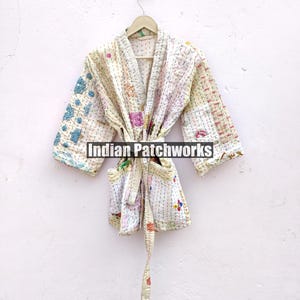 K&ouml;nnte beinhalten: Eine wei&szlig;e Baumwollrobe mit Patchwork-Muster und einem Bindeg&uuml;rtel. Die Robe hat ein hellblaues und rosafarbenes Blumenmuster. Der Text "Indian Patchworks" ist auf der Robe sichtbar.