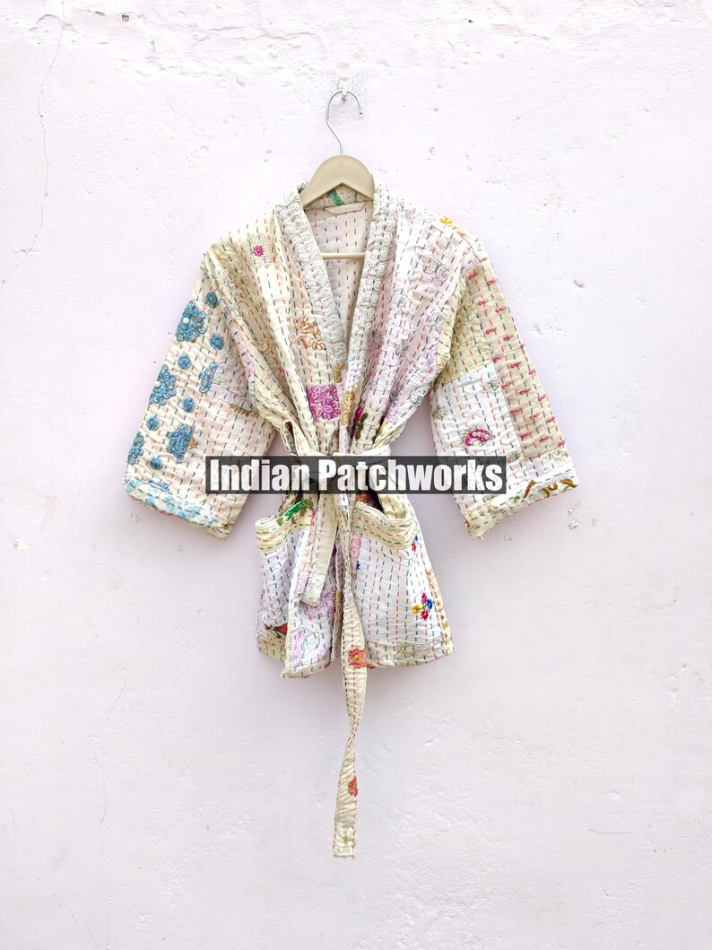 K&ouml;nnte beinhalten: Eine wei&szlig;e Baumwollrobe mit Patchwork-Muster und einem Bindeg&uuml;rtel. Die Robe hat ein hellblaues und rosafarbenes Blumenmuster. Der Text "Indian Patchworks" ist auf der Robe sichtbar.