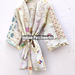 K&ouml;nnte beinhalten: Eine wei&szlig;e gesteppte Robe mit bunten Blumenstickereien und einem Bindeg&uuml;rtel. Die Robe ist aus Patchwork-Stoff gefertigt und hat eine lockere Passform. "Indian Patchworks" ist auf die Robe gedruckt.
