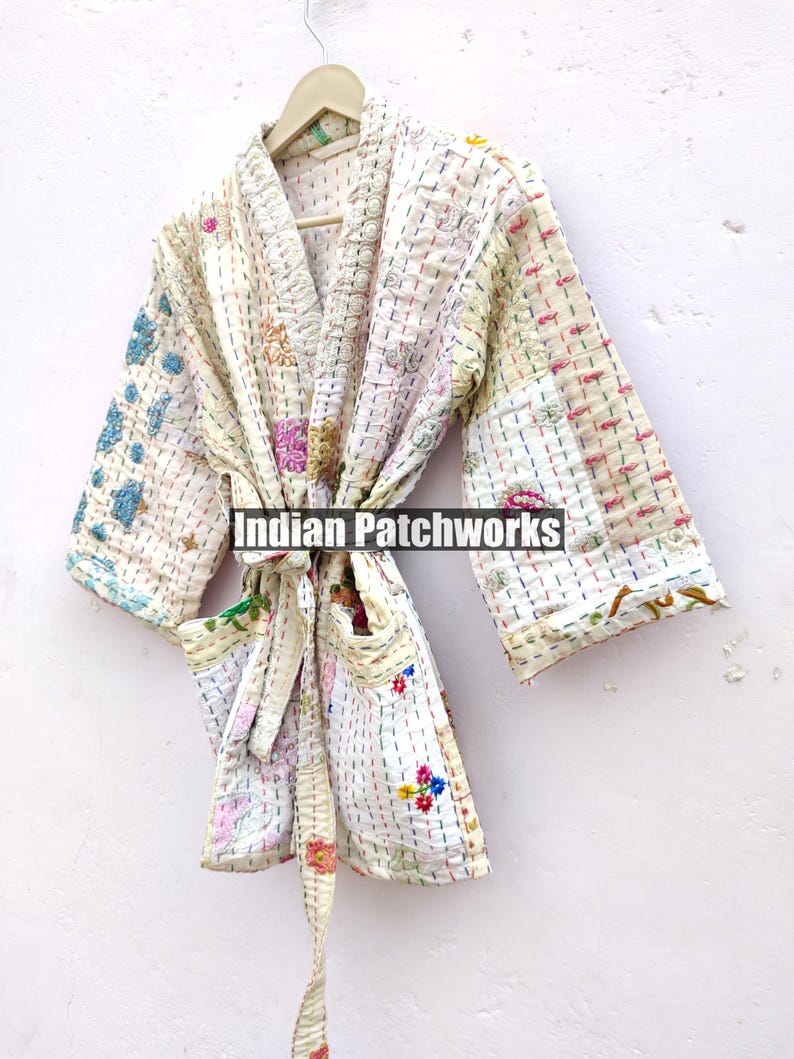 K&ouml;nnte beinhalten: Eine wei&szlig;e gesteppte Robe mit bunten Blumenstickereien und einem Bindeg&uuml;rtel. Die Robe ist aus Patchwork-Stoff gefertigt und hat eine lockere Passform. "Indian Patchworks" ist auf die Robe gedruckt.