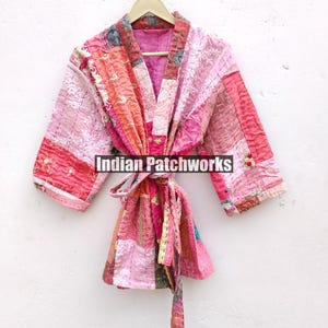 May include: A pink and red patchwork quilted kimono with a long tie belt. The kimono has a V-neck and is made of a soft, lightweight fabric. "Indian Patchworks" is printed on the front of the kimono.