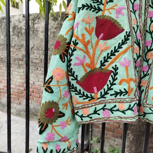 May include: A mint green embroidered jacket with colorful floral patterns. The jacket has a long sleeve and a button closure.
