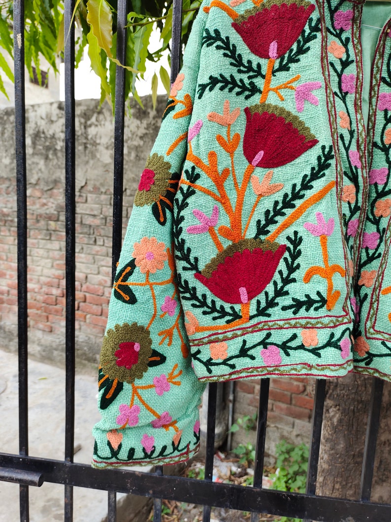 May include: A mint green embroidered jacket with colorful floral patterns. The jacket has a long sleeve and a button closure.