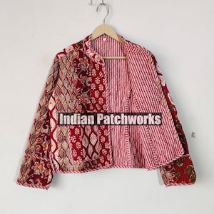 Peut inclure: Une veste matelassée rouge, blanche et bleue avec un motif floral. La veste a un col mandarin et une fermeture à boutons. Le texte "Indian Patchworks" est imprimé sur le devant de la veste.