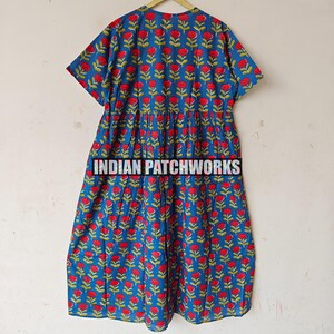 May include: A blue dress with a red floral pattern and green stems hangs on a wooden hanger. The dress has short sleeves and a gathered waist. The text "INDIAN PATCHWORKS" is printed across the bottom of the dress.