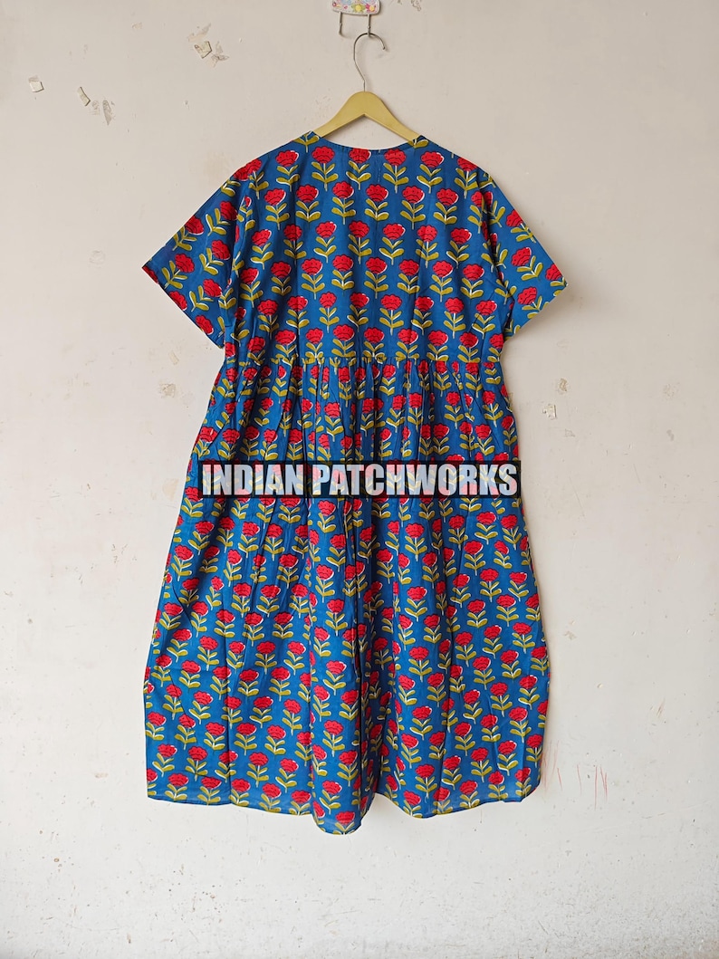 May include: A blue dress with a red floral pattern and green stems hangs on a wooden hanger. The dress has short sleeves and a gathered waist. The text "INDIAN PATCHWORKS" is printed across the bottom of the dress.