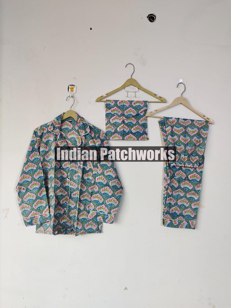 May include: A three-piece pajama set with a floral pattern in shades of teal, pink, and white. The set includes a button-down shirt, a pair of pants, and a matching eye mask, all hanging on wooden hangers. The text "Indian Patchworks" is visible.