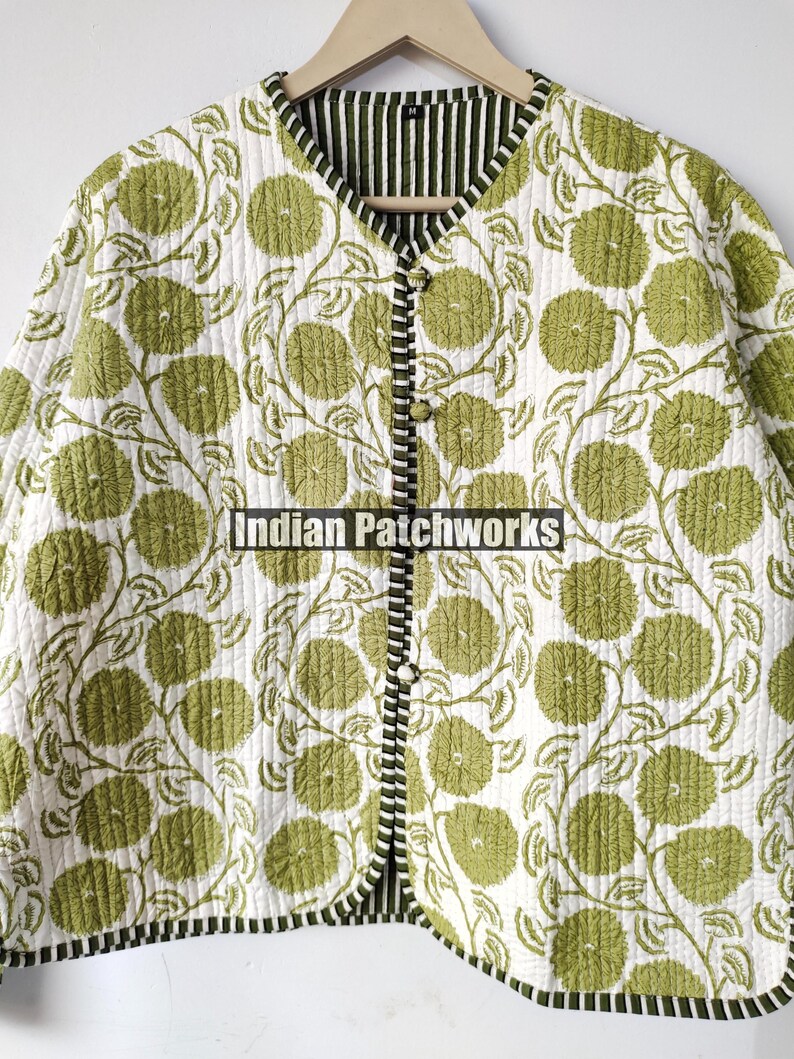 May include: A quilted jacket featuring a floral design in green on a white backdrop. The jacket has a V-neck, button closure, and black and white striped trim. The text "Indian Patchworks" is visible.