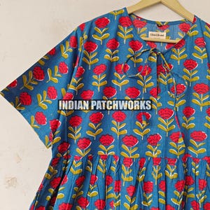 May include: A blue dress featuring a repeating pattern of red flowers with yellow stems. The dress has short sleeves and a tie at the neckline. The text "INDIAN PATCHWORKS" is across the front.