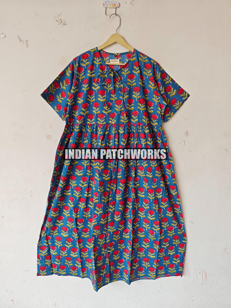 May include: Blue dress featuring a red floral print and short sleeves. The dress has a gathered waist and a button-up neckline. The text "INDIAN PATCHWORKS" is visible at the bottom of the dress.