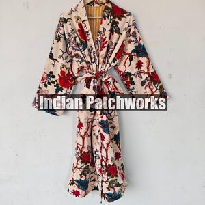 May include: A white cotton robe with a floral print in shades of red, blue, and green. The robe has a tie belt and a yellow and white striped lining. The text "Indian Patchworks" is visible on the robe.