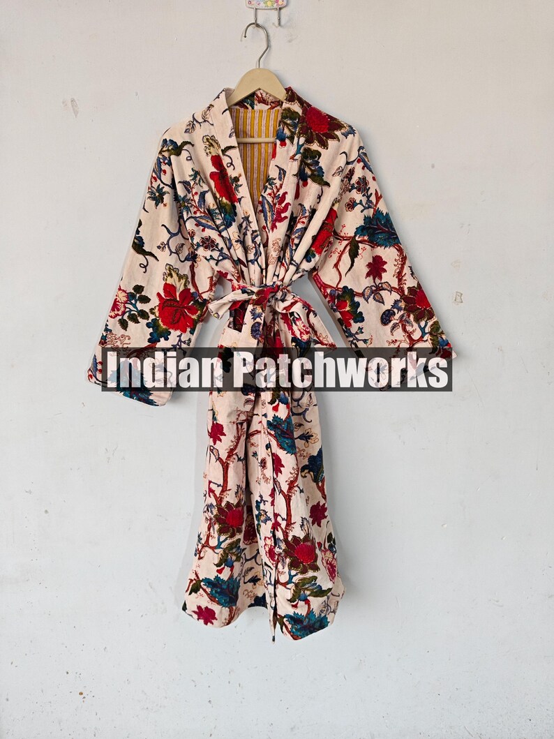 May include: A white cotton robe with a floral print in shades of red, blue, and green. The robe has a tie belt and a yellow and white striped lining. The text "Indian Patchworks" is visible on the robe.
