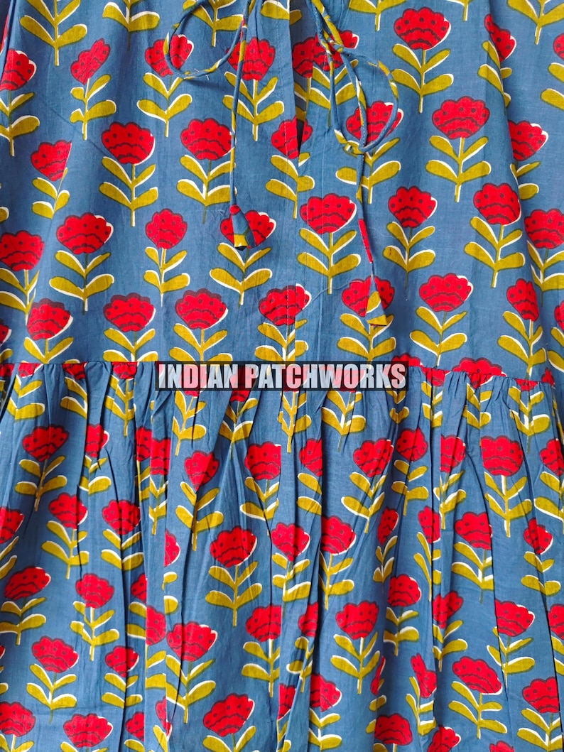 May include: Close-up of a blue fabric with a repeating floral pattern. Red flowers with yellow stems and green leaves are printed on the fabric. The text "INDIAN PATCHWORKS" is printed across the fabric.