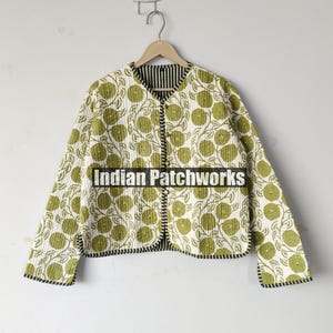 May include: A quilted jacket with a floral pattern in shades of green and white. The jacket has a black and white striped lining and black trim. The text "Indian Patchworks" is printed on the front.