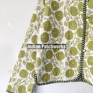May include: A quilted jacket featuring a green floral design on a white backdrop. The jacket has a black and white striped trim and the text "Indian Patchworks".
