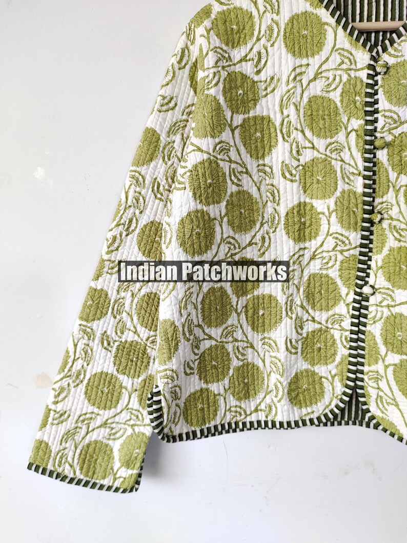May include: A quilted jacket featuring a green floral design on a white backdrop. The jacket has a black and white striped trim and the text "Indian Patchworks".