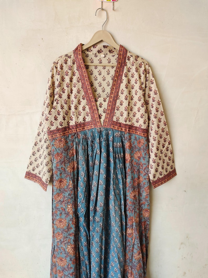 May include: A long, cream-colored dress with a V-neckline and long sleeves. The dress has a floral print in shades of brown, blue, and cream. The dress is made of a lightweight fabric and has a relaxed fit.