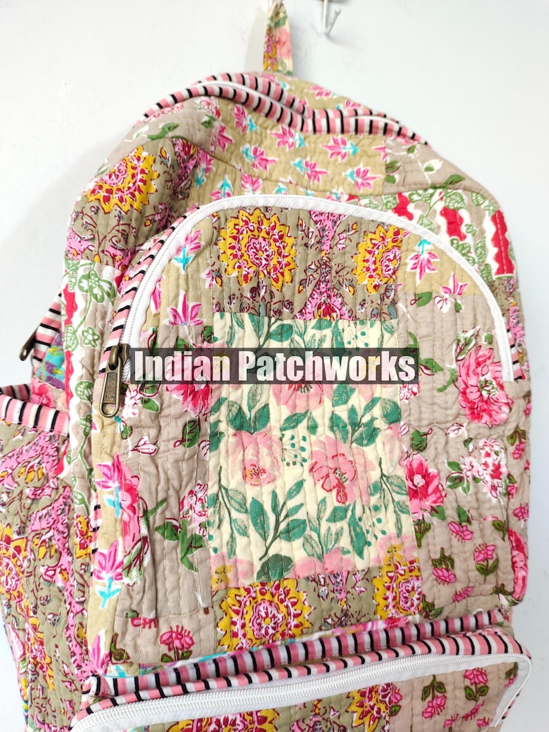 May include: A quilted backpack with a floral patchwork design. The bag features a beige background with pink, yellow, and green floral patterns. The text "Indian Patchworks" is printed on the front pocket.