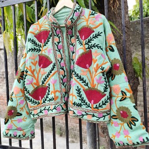 May include: A mint green embroidered jacket with floral patterns in shades of red, orange, pink, and green. The jacket has a mandarin collar and a front closure.