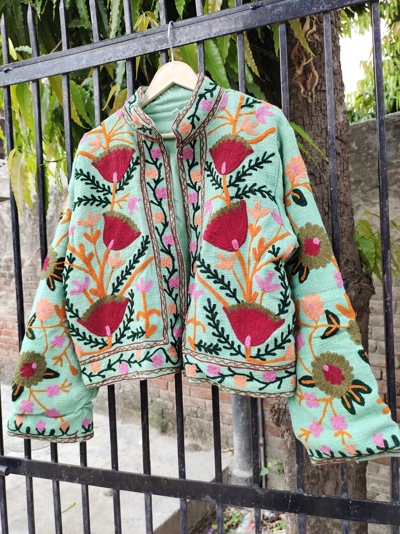 May include: A mint green embroidered jacket with floral patterns in shades of red, orange, pink, and green. The jacket has a mandarin collar and a front closure.