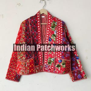 May include: A red quilted jacket with a floral patchwork design. The jacket has long sleeves and a collarless neckline. The jacket is made of cotton and is lined with a red and white striped fabric.