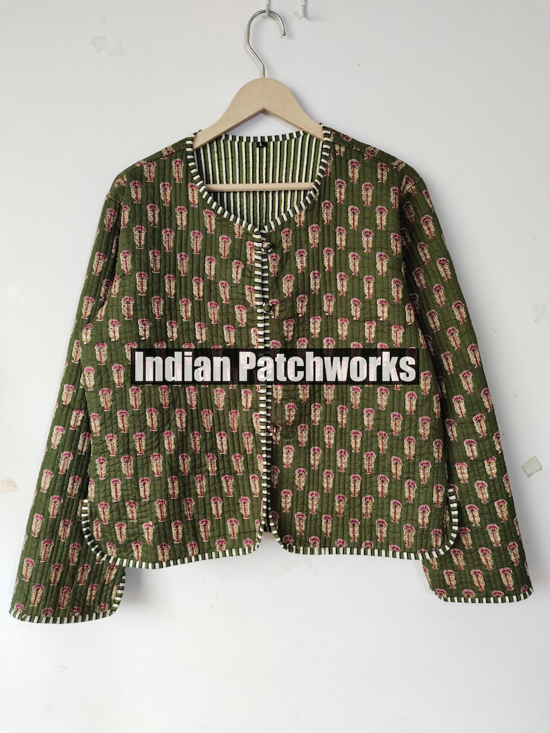 May include: Olive green quilted jacket with a floral pattern in pink and white. The jacket has a striped lining and trim. The text "Indian Patchworks" is printed on the front of the jacket.