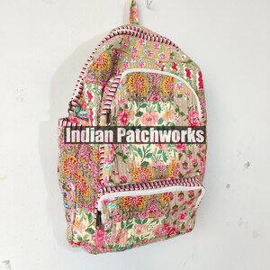May include: A quilted backpack with a floral pattern in pink, yellow, and green on a tan background. The backpack has white zippers, pink and white striped trim, and the text "Indian Patchworks" across the front.