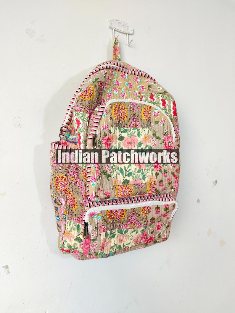 May include: A quilted backpack with a floral pattern in pink, yellow, and green on a tan background. The backpack has white zippers, pink and white striped trim, and the text "Indian Patchworks" across the front.