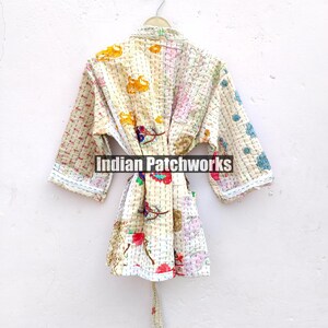 K&ouml;nnte beinhalten: Eine wei&szlig;e Baumwollrobe mit einem floralen Patchwork-Muster. Die Robe hat einen Bindeg&uuml;rtel und lange &Auml;rmel. Der Text "Indian Patchworks" ist auf der Robe sichtbar.