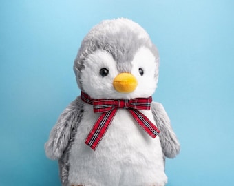 May include: A plush penguin toy with soft grey and white fur, a bright yellow beak, and yellow feet. The penguin wears a red, green, and white plaid ribbon bow around its neck. Above the toy, the text reads Furrful Prima the Penguin.