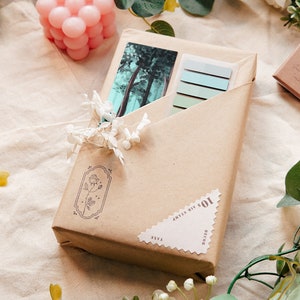 May include: A brown paper package with a vintage postcard inside. The package is decorated with a floral stamp and a sticker that says "101 days til my b-day".