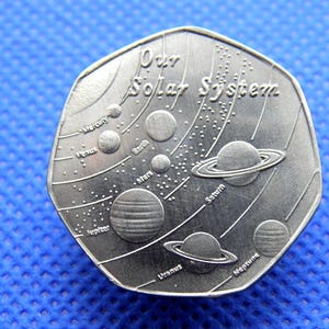 Puede incluir: Una moneda plateada con la inscripción "Our Solar System" e ilustraciones de los planetas. La moneda muestra Mercurio, Venus, Tierra, Marte, Júpiter, Saturno, Urano y Neptuno. La moneda está sobre un fondo azul.