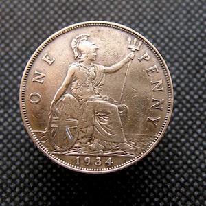 Op de afbeelding: Een koperen Britse munt van één penny met de afbeelding van een zittende vrouw die een drietand vasthoudt en de tekst "ONE PENNY" rond de rand. Het jaar 1934 is onderaan gegraveerd.