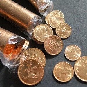 Może przedstawiać: Zbliżenie brytyjskich monet, w tym pensów i dziesięciopensówek, niektóre w rolkach, inne rozrzucone. Monety mają miedziano-złoty kolor, z wizerunkami królowej Elżbiety II i innymi wzorami.