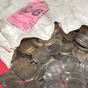 May include: A white cloth bag filled with silver coins. The bag has a pink tag attached to it that reads "365 Half Crowns, £100 oz."