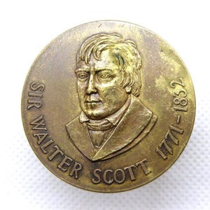 Puede incluir: Medalla redonda de bronce antiguo con un retrato de Sir Walter Scott. El texto "SIR WALTER SCOTT" está inscrito en la parte superior e izquierda. Las fechas "1771-1832" están inscritas en el lado derecho. La medalla tiene un aspecto desgastado y envejecido.