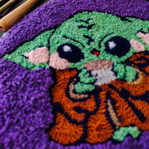 May include: A close-up of a purple, green, orange, and pink rug with a cartoon character design. The rug is made of yarn and has a fuzzy texture.