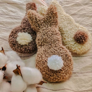 May include: Three plush bunny-shaped hand warmers in brown, beige, and white. Each warmer has a fluffy pom-pom tail.