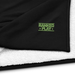 May include: Black blanket with a white sherpa lining. The blanket has the words "RANKED PLAY" embroidered in green with a star on each side. The blanket is folded over, showing the soft, fluffy lining.