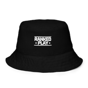 May include: Black bucket hat with the text "RANKED PLAY" in white block letters. The text is centered on the front of the hat, above a white horizontal line, with a star on each side of the word "PLAY".
