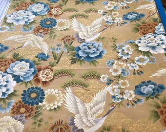 May include: A roll of fabric with a gold background featuring a floral and bird design. The pattern includes white cranes, blue and white peonies, and other flowers. The fabric is likely used for sewing or crafting projects.