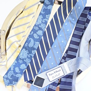 May include: A silver tray with a collection of blue and yellow patterned neckties. A white tag with the text "Kate & Brad 11.05.17" is attached to one of the ties.