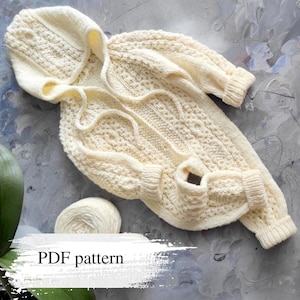 May include: Cream-coloured knitted baby sweater with a hood and intricate cable knit detailing. The sweater has long sleeves, pockets, and a drawstring. A ball of yarn is next to the sweater. The text "PDF pattern" is visible.