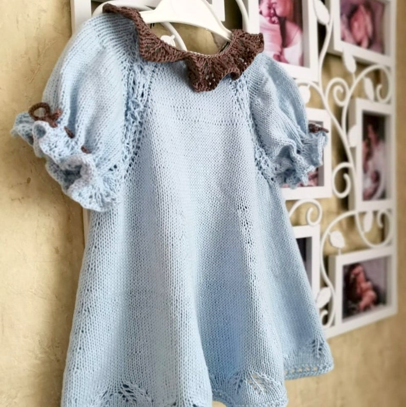 May include: A light blue knitted baby dress with a brown crocheted collar and ruffled sleeves.