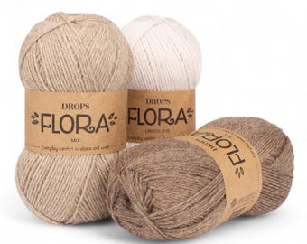 Könnte beinhalten: Drei Knäuel Drops Flora-Garn in neutralen Farben. Das Garn ist mit dem Markennamen und Produktdetails versehen. Die Farben umfassen Beige, Weiß und Braun. Das Garn besteht aus Alpaka und Wolle.